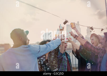 Jeunes adultes enthousiastes friends toasting cocktails at rooftop party Banque D'Images