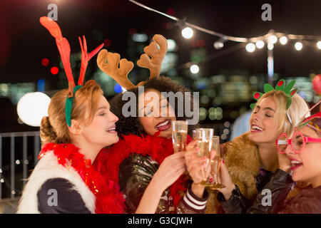 Les jeunes femmes portant des bois de renne de Noël et toasting champagne glasses at rooftop party Banque D'Images