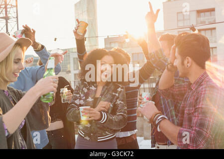 Les amis des jeunes adultes enthousiastes dansant et buvant at rooftop party Banque D'Images