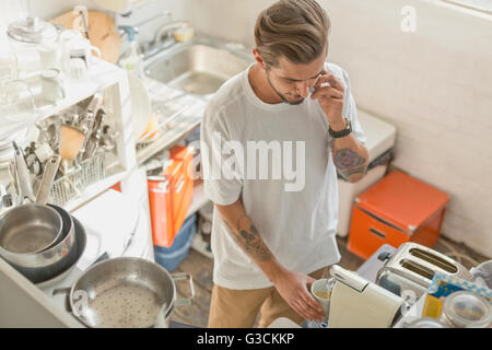 L'homme à l'aide de la machine à expresso et talking on cell phone in Cuisine de l'appartement Banque D'Images