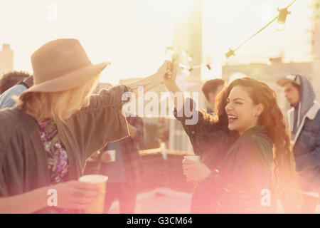 Les jeunes femmes adultes enthousiastes dansant et buvant at rooftop party Banque D'Images