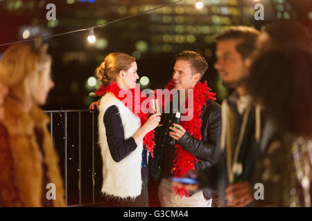 Jeune couple drinking champagne at rooftop party la nuit Banque D'Images