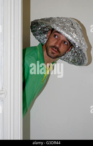Théorie du complot mâle croyant vêtu d'aluminium hat scrutant de porte Banque D'Images