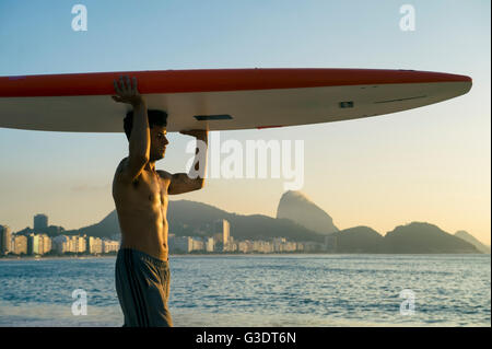 RIO DE JANEIRO - 5 avril, 2016 : un jeune homme brésilien sur la plage de Copacabana, équilibre un surf en face de Sugarloaf Mountain. Banque D'Images