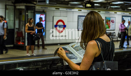 Femme lisant un journal sur le quai de la station de métro Victoria, en attendant un train, Londres, Royaume-Uni Banque D'Images