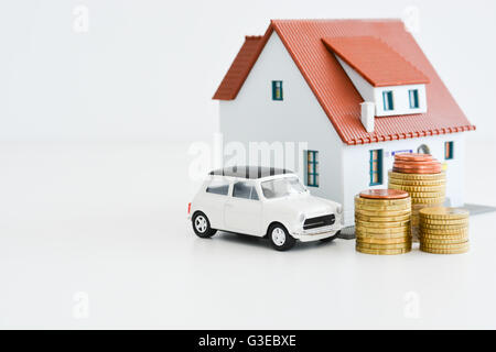 Voiture et la maison modèle avec pile de pièces isolées sur fond blanc Banque D'Images
