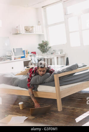Young man laying on bed using laptop in vacances Banque D'Images