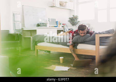 Young man laying on bed using laptop in vacances Banque D'Images