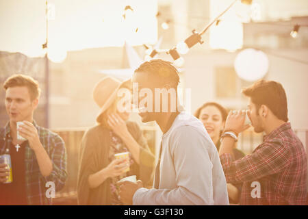 Jeune homme de rire et de boire at rooftop party Banque D'Images