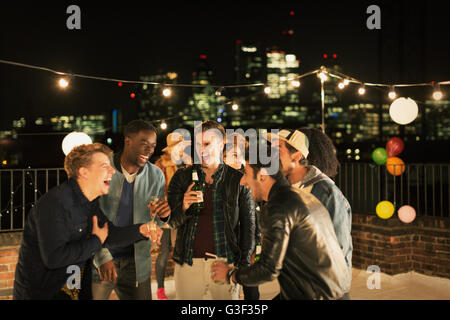 Les jeunes hommes buvant et riant at rooftop party Banque D'Images