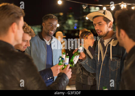 Young adult friends toasting beer bottles at rooftop party Banque D'Images