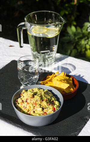 Guacamole fait maison dans un bol en céramique et des croustilles tortillas et la crème aigrie sur le côté avec verseuse en verre et d'eau glacée. Sur ardoise m Banque D'Images