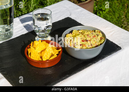 Guacamole fait maison dans un bol en céramique et des croustilles tortillas et la crème aigrie sur le côté avec verseuse en verre et d'eau glacée. Sur ardoise m Banque D'Images