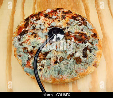 Vieux stéthoscope et pizza moisi sur une table en bois. L'intoxication alimentaire Banque D'Images