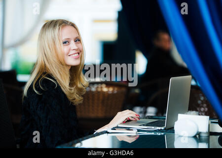 Portrait de très jolie jeune femme assise au café de la rue avec son portable, la dactylographie et smiling Banque D'Images