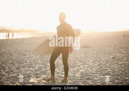 Male surfer carrying surfboard on sunlit Venice Beach, Californie, USA Banque D'Images