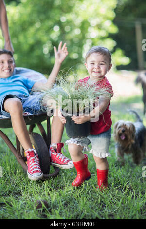 Young Girl holding plant, son frère est poussée dans une brouette Banque D'Images