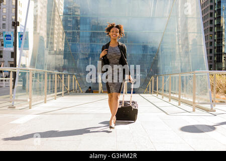 Businesswoman walking outdoors, tirant valise à roulettes Banque D'Images