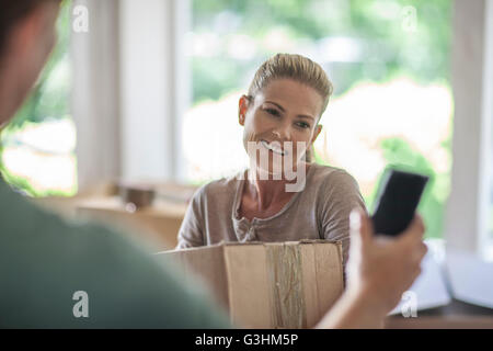 Déménagement : woman holding boîte carton, man holding smartphone Banque D'Images