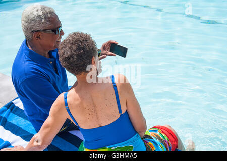 Couple assis à côté d'une piscine, using smartphone Banque D'Images