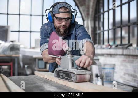 Carpenter avec ponçage à bande dans l'atelier de restauration d'antiquités Banque D'Images