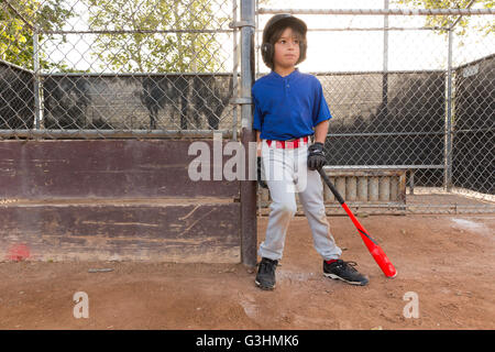 Boy leaning against fence with baseball bat à l'entraînement sur le terrain de baseball Banque D'Images