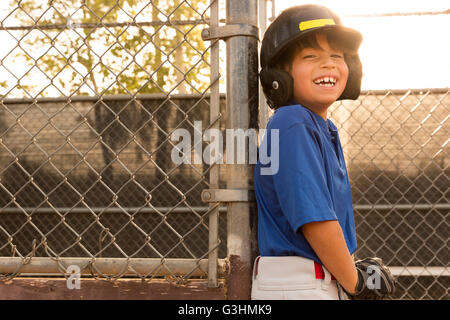 Laughing boy leaning against clôture à l'entraînement de base-ball Banque D'Images