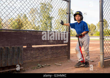Portrait of boy with baseball bat appuyé contre clôture à l'entraînement de base-ball Banque D'Images
