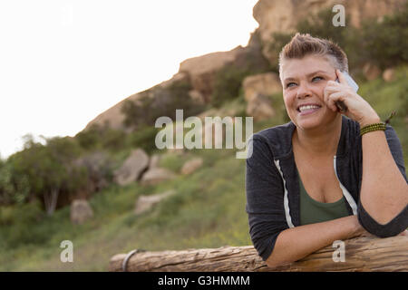 Court-haired woman leaning against fence using smartphone Banque D'Images