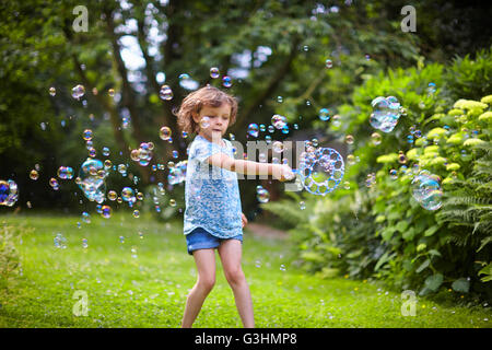 Girl waving bubble wand et faire des bulles dans le jardin Banque D'Images