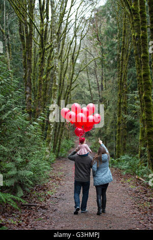 Vue arrière des parents exerçant son tout-petit fille sur les épaules avec des tas de ballons rouges dans la forêt Banque D'Images