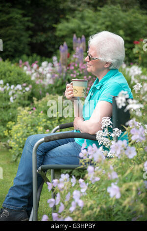 Dame mature est assis dans le jardin avec une tasse de thé et un air pensif, réfléchissant expression sur son visage. Banque D'Images