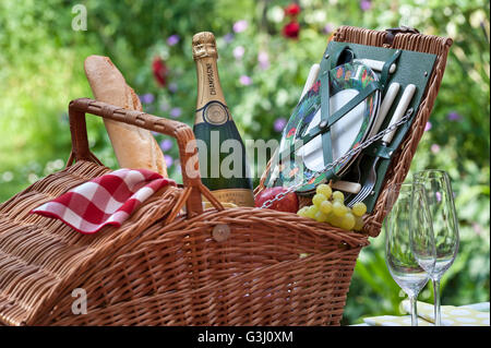 Bouteille de champagne français et raisins pain panier pique-nique en osier dans alfresco floral ensoleillé situation Banque D'Images