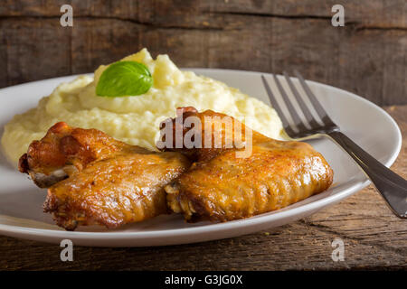 Ailes de poulet frit et sa purée de pommes de terre sur la plaque avec la fourchette sur fond de bois Banque D'Images