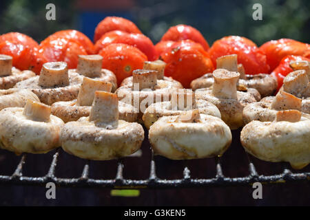 Dans les légumes de sel, d'épices et de la cuisson sur gril extérieur, char white champignons portobellos et petites tomates rouges Banque D'Images