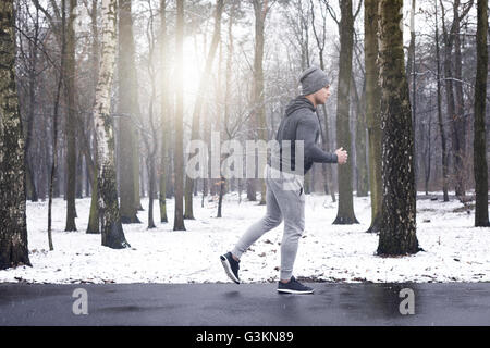 Young man jogging à travers la forêt enneigée Banque D'Images