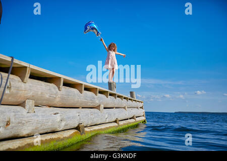 Jeune fille debout sur un post sur pier, holding hélium ballon Banque D'Images