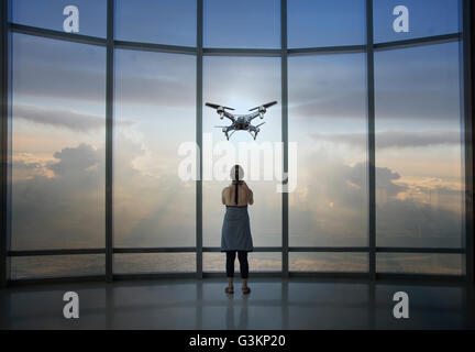 Full Length rear view of woman watching drone depuis la fenêtre gratte-ciel Banque D'Images