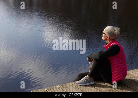 Vue latérale du woman sitting on wooden pier looking away Banque D'Images