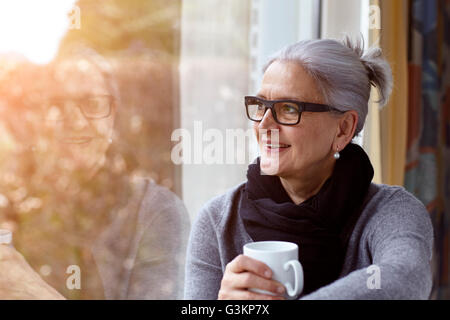Woman wearing glasses holding Coffee cup à la fenêtre de Banque D'Images