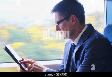 Mature businessman sitting on train, using digital tablet Banque D'Images