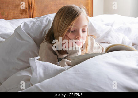 Fille aux cheveux blonds reading book in bed Banque D'Images