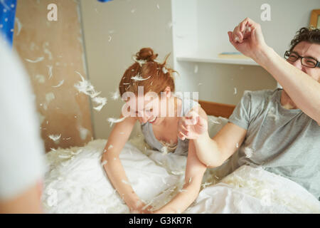 Young couple having pillow fight with daughter in bed Banque D'Images