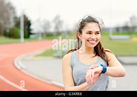 Jeune femme à côté d'une piste de course, contrôle watch, smiling Banque D'Images