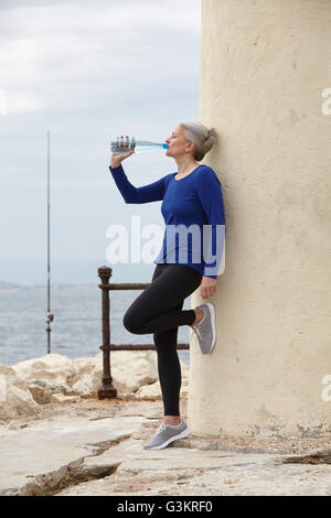 Femme mature en plein air, leaning against wall, bouteille d'eau potable à partir de Banque D'Images