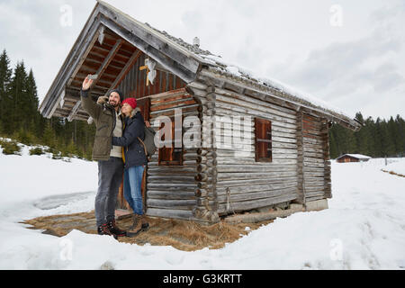 Couple en tenant l'extérieur selfies smartphone log cabin en hiver, Elmau, Bavière, Allemagne Banque D'Images