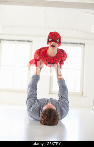 Père lying on floor holding up fils wearing superhero costume Banque D'Images