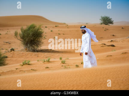 Middle Eastern homme portant des vêtements traditionnels walking in desert, Dubaï, Émirats Arabes Unis Banque D'Images