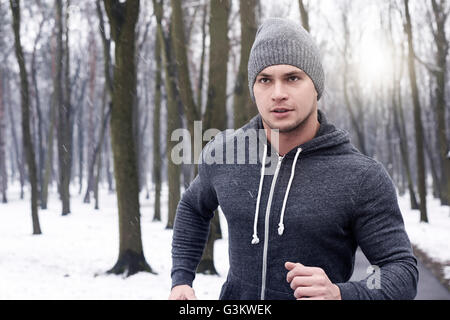 Young man jogging à travers la forêt enneigée Banque D'Images