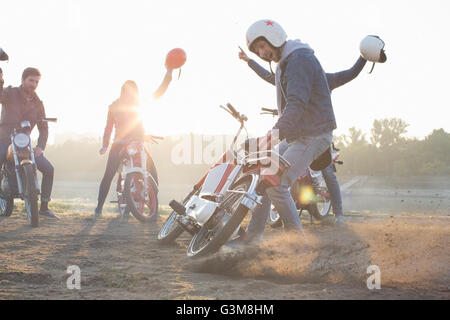 Petit groupe d'amis assis sur les cyclomoteurs, holding casques dans l'air Banque D'Images